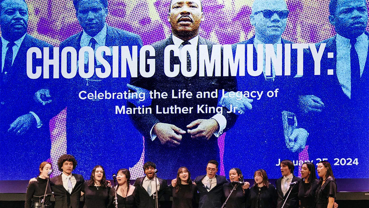 Acapella group performing in front of a large image of MLK linking arms with marchers and the words "Choosing Community"